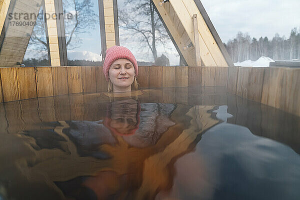 Frau mit geschlossenen Augen entspannt sich im Whirlpool vor dem Haus