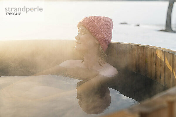 Oben-ohne-Frau mit Strickmütze nimmt im Winter ein heißes Wasserbad