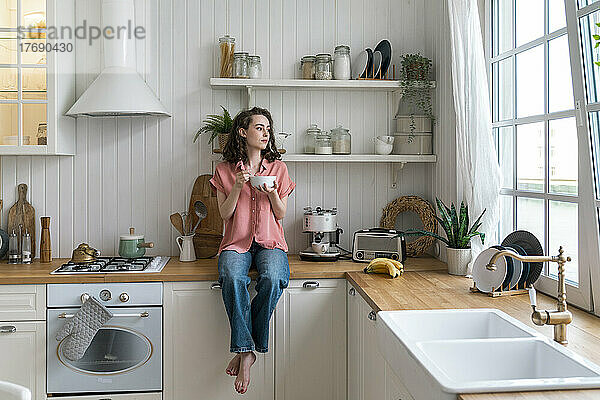 Frau mit Schüssel sitzt zu Hause auf der Küchentheke
