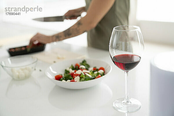 Weinglas auf Kücheninsel  im Hintergrund bereitet Frau zu Hause Essen zu