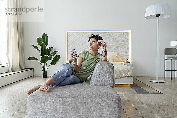 Frau benutzt Mobiltelefon und sitzt zu Hause auf dem Sofa