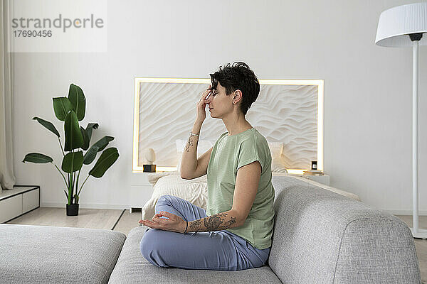Meditierende Frau sitzt zu Hause auf dem Sofa