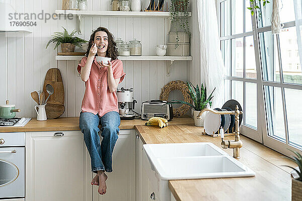 Frau sitzt zu Hause auf der Küchentheke und frühstückt