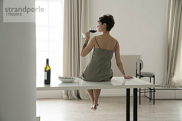 Frau trinkt Rotwein und sitzt zu Hause am Tisch