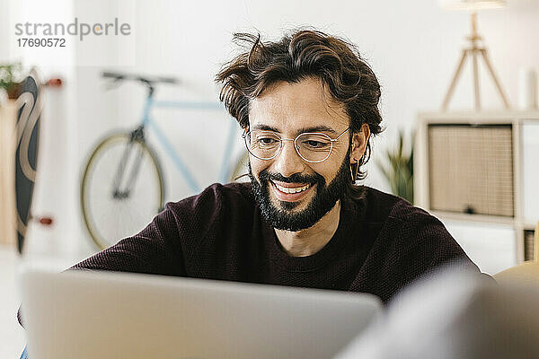 Lächelnder Mann mit Brille und Laptop im heimischen Wohnzimmer