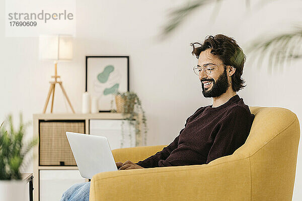 Lächelnder Mann mit Laptop  der zu Hause auf dem Sofa sitzt