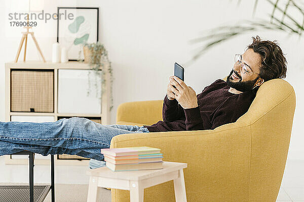 Entspannter Mann  der zu Hause auf dem Sofa sitzt und sein Smartphone benutzt