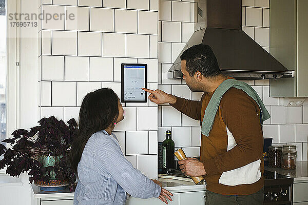 Mädchen schaut Vater an  der in der Küche zu Hause ein Hausautomatisierungsgerät benutzt