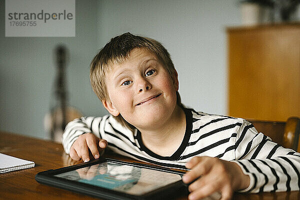 Porträt eines glücklichen Jungen mit Down-Syndrom  der am Tisch sitzt