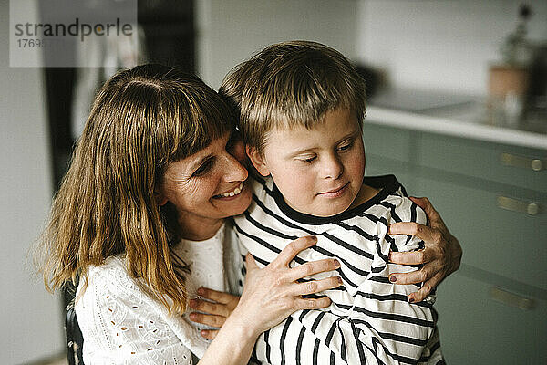 Glückliche Mutter umarmt ihren behinderten Sohn zu Hause