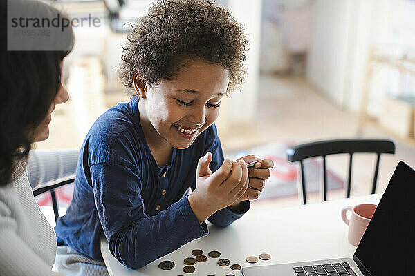 Glücklicher Junge schaut auf seine Kreditkarte  während er mit seiner Mutter zu Hause sitzt