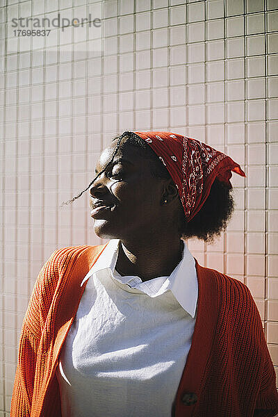 Lächelnde Frau mit Kopftuch steht mit geschlossenen Augen an einem sonnigen Tag