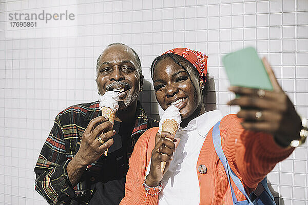 Lächelnder Mann  der ein Selfie mit seinem Vater macht und an einem sonnigen Tag ein Eis isst