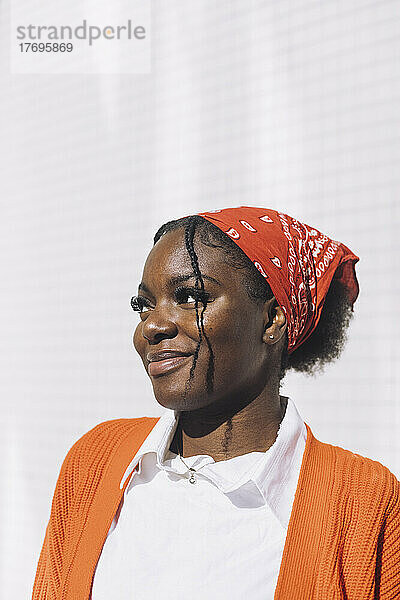 Lächelnde junge Frau mit Kopftuch  die an einem sonnigen Tag an der Wand steht