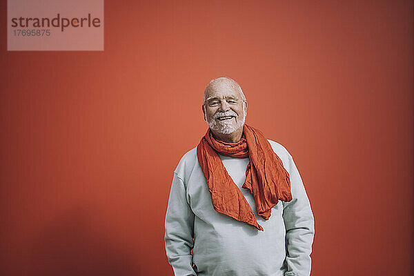 Porträt eines glücklichen älteren Mannes  der vor einem orangefarbenen Hintergrund steht