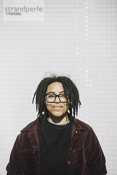 Porträt einer lächelnden Genderqueer-Person mit Brille  die an einer Wand steht