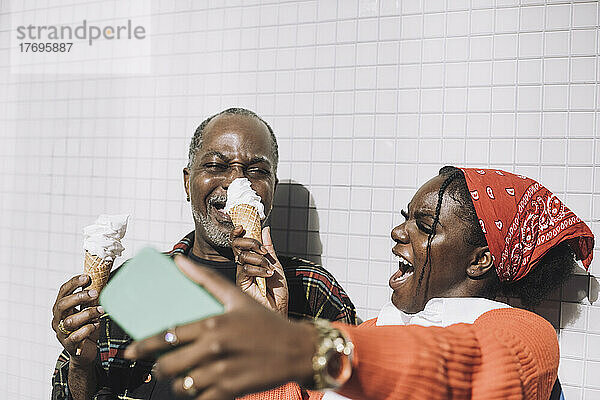 Fröhliche Frau  die ein Selfie mit ihrem Handy macht  während sie sich mit ihrem Vater an einem sonnigen Tag über ein Eis freut
