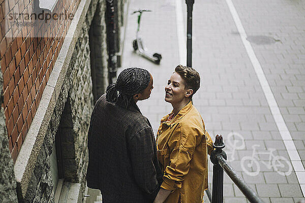 Lächelnde erwachsene Frau im Gespräch mit ihrer Freundin  während sie am Geländer steht