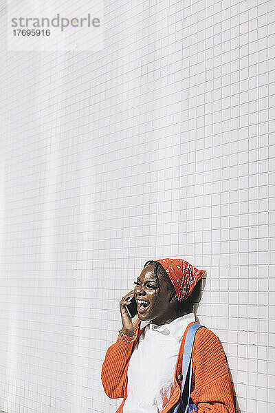 Junge Frau lacht  während sie mit einem Mobiltelefon an der Wand spricht