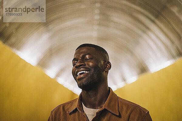 Junger Mann lachend mit geschlossenen Augen in beleuchtetem Tunnel