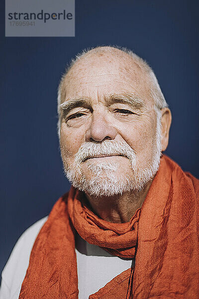 Porträt eines älteren Mannes mit orangefarbenem Schal vor blauem Hintergrund
