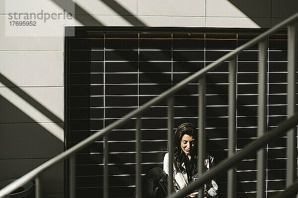 Geschäftsfrau sitzt an der Wand eines Bahnhofs an einem sonnigen Tag