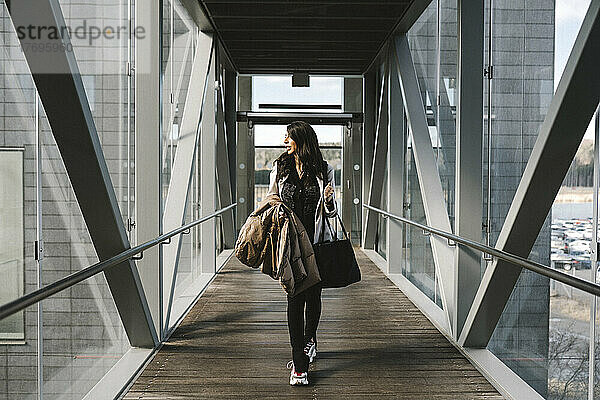 Geschäftsfrau schaut weg und hält eine Tasche  während sie auf einer Fußgängerbrücke geht