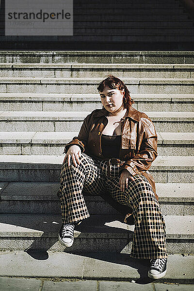 Porträt einer selbstbewussten jungen Frau auf einer Treppe sitzend an einem sonnigen Tag