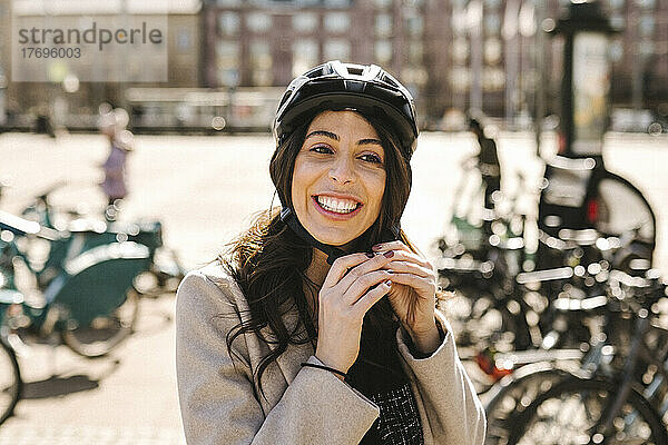 Glückliche Geschäftsfrau mit Helm an einer Fahrradabstellanlage in der Stadt