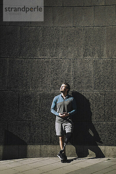 Mann mit Behinderung  der an einem sonnigen Tag an der Wand stehend nach oben schaut