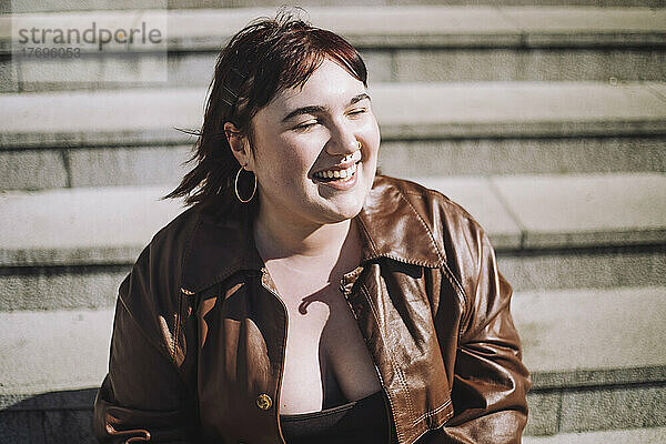 Glückliche junge Frau mit geschlossenen Augen auf einer Treppe sitzend an einem sonnigen Tag