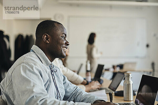 Seitenansicht eines lächelnden männlichen Schülers mit Laptop im Klassenzimmer