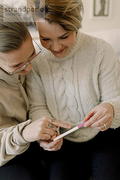 Neugieriges lesbisches Paar betrachtet die Ergebnisse eines Schwangerschaftstests