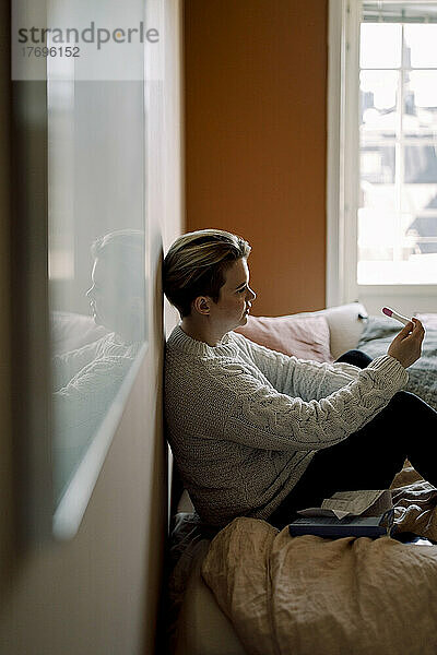 Depressive junge lesbische Frau mit Schwangerschaftstestergebnissen  die zu Hause auf dem Bett sitzt