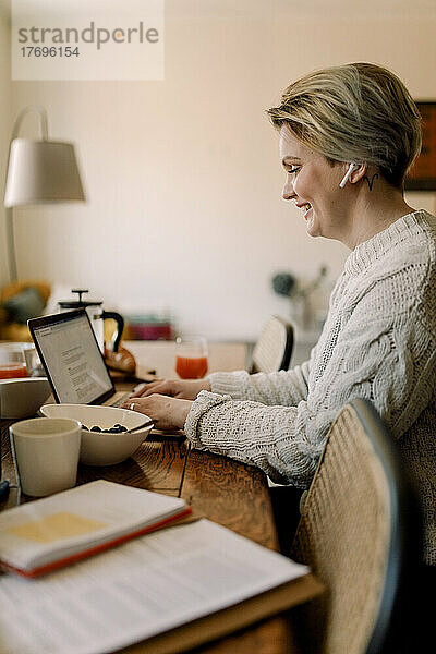 Seitenansicht einer lesbischen Geschäftsfrau mit Laptop am Esstisch sitzend