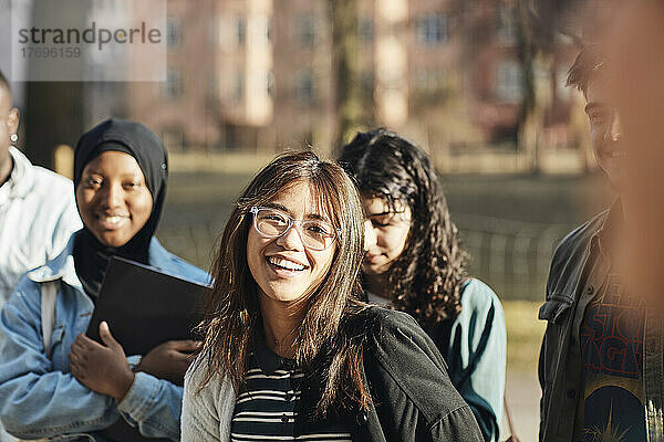Porträt einer lächelnden jungen Studentin mit Freunden auf dem Universitätscampus an einem sonnigen Tag