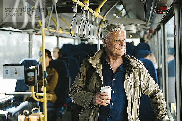 Nachdenklicher Geschäftsmann hält Einwegbecher beim Pendeln im Bus