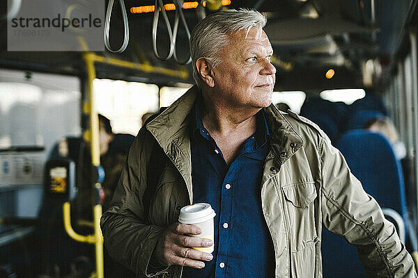 Geschäftsmann schaut weg und hält einen Einwegbecher  während er im Bus steht
