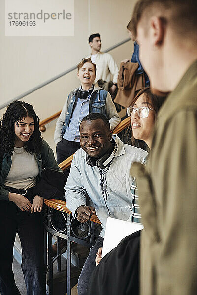 Glückliche junge gemischtrassige Studenten  die sich im Treppenhaus einer Universität vergnügen