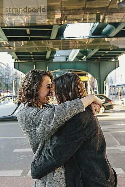 Fröhliches lesbisches Paar  das sich umarmt  während es auf der Straße unter einer Brücke in der Stadt steht