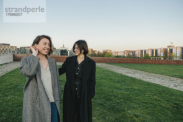 Lächelndes lesbisches Paar geht im Park gegen den klaren Himmel