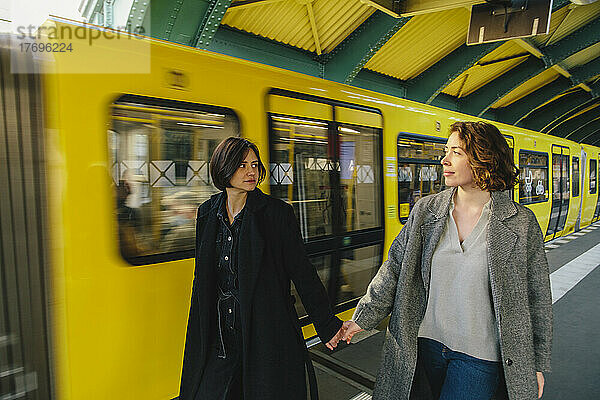 Lesbisches Paar geht Hand in Hand mit einem gelben Zug am Bahnhof