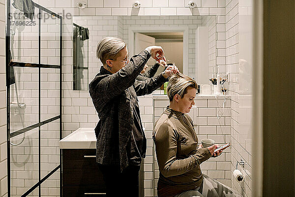 Seitenansicht einer lesbischen Frau  die ihrer Freundin im Badezimmer zu Hause die Haare schneidet
