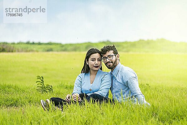 Porträt eines verliebten Paares  das im Gras auf einem Feld sitzt  Romantisches Paar  das im Gras sitzt und in die Kamera schaut  Zwei Liebende  die im Gras sitzen und in die Kamera schauen