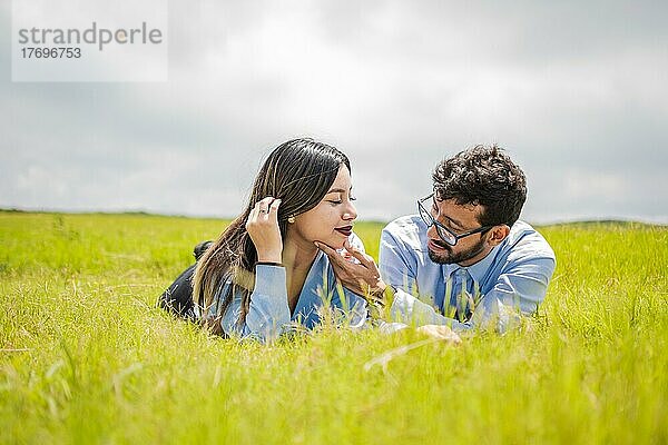 Ein Paar  das im Gras liegt und sich anschaut  ein junges verliebtes Paar  das im Gras liegt und sich gegenseitig berührt  zwei verliebte Menschen  die im Gras liegen und sich anschauen