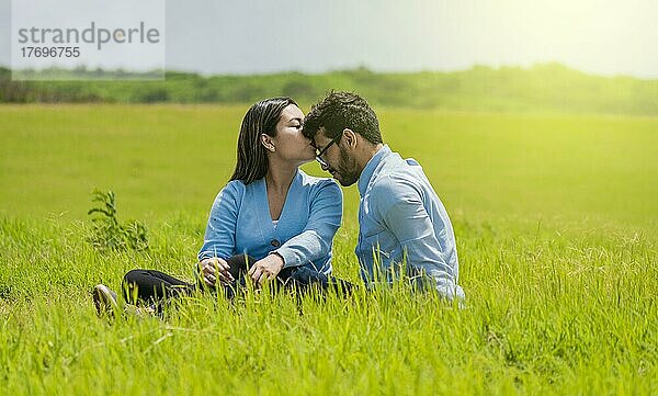 Romantisches Paar sitzt im Gras und küsst sich auf die Stirn  Ein hübsches Mädchen küsst die Stirn ihres Freundes auf dem Feld  Ein verliebtes Paar sitzt auf dem Feld und küsst sich auf die Stirn