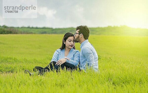 Ein verliebtes Paar sitzt im Feld und küsst sich auf die Stirn  Ein Mann küsst seine Freundin auf die Stirn im Feld  Romantisches Paar sitzt im Gras und küsst sich auf die Stirn