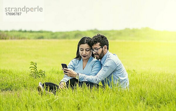 Junges verliebtes Paar macht ein Selfie auf dem Feld  Zwei Verliebte sitzen im Gras und machen Selfies  Verliebte machen Selfies auf dem Feld mit ihrem Smartphone