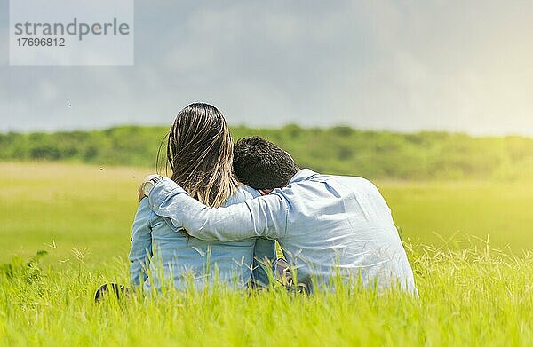 Ein verliebtes Paar sitzt auf dem Gras und umarmt sich von hinten  ein romantisches Paar sitzt auf dem Gras und umarmt sich von hinten  Rückansicht eines verliebten Paares  das sich auf dem Gras umarmt