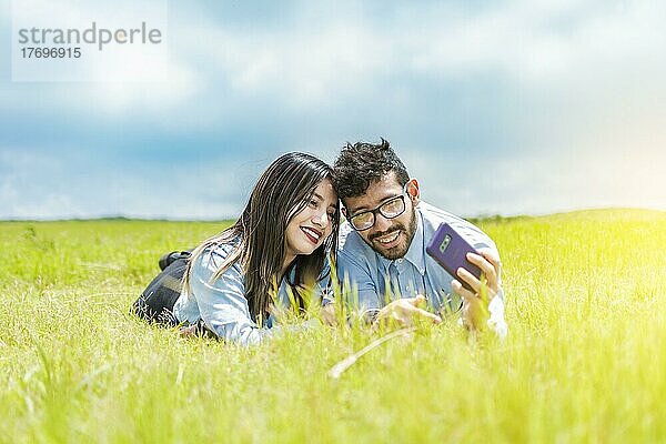 Ein Paar  das im Gras liegt und ein Selfie macht  ein junges verliebtes Paar  zwei verliebte Menschen  die im Gras liegen und Selfies machen